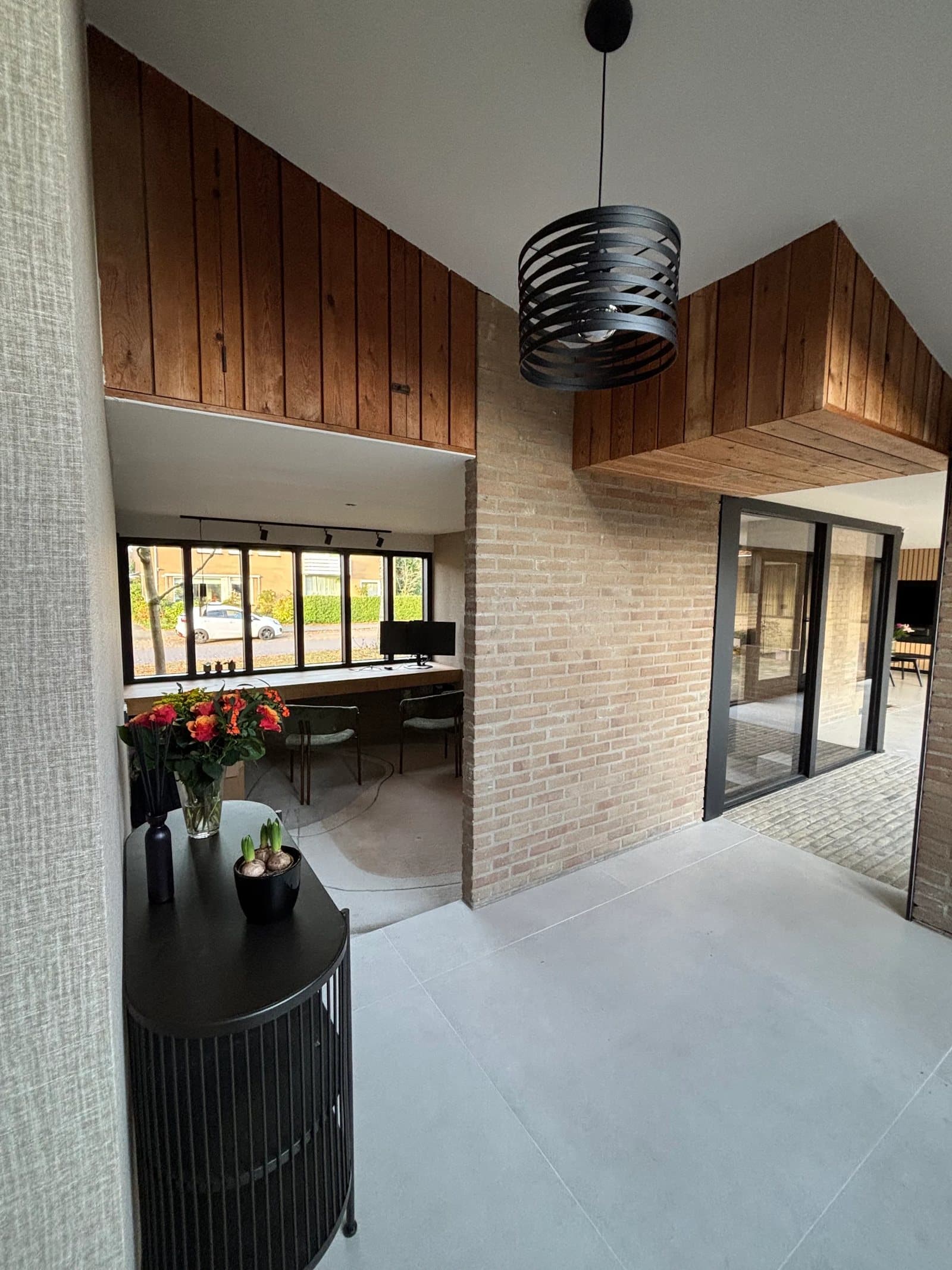 Hal met houten bekleding onder het flauwe dak, gele baksteen en doorkijk naar de werkkamer in een Van Zantinge-villa