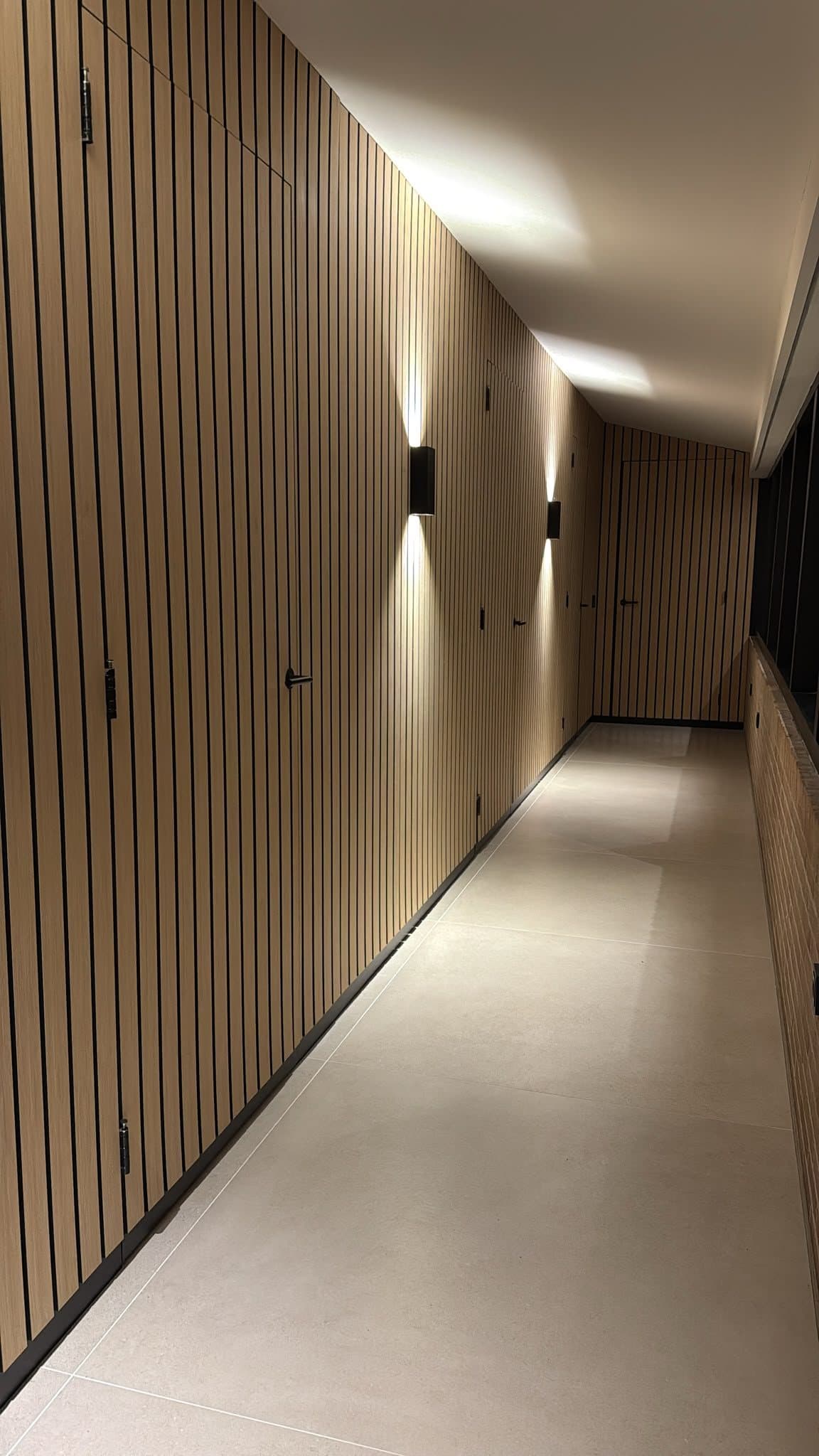 Gang met maatwerk wandbekleding van houten lamellen, weggewerkte deuren en wandlampen