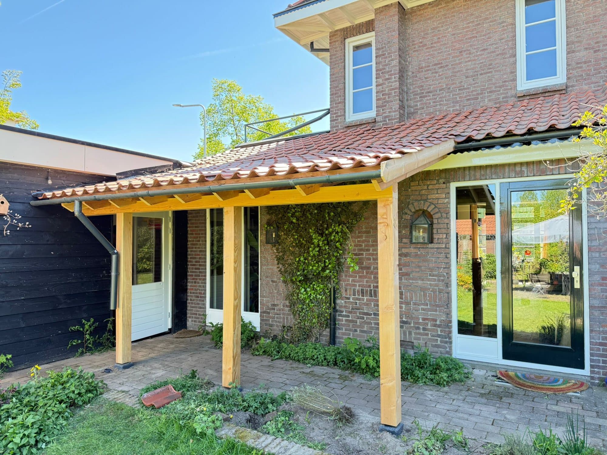 Nieuwe houten veranda met rode dakpannen in het verlengde van een bakstenen woning in Almelo